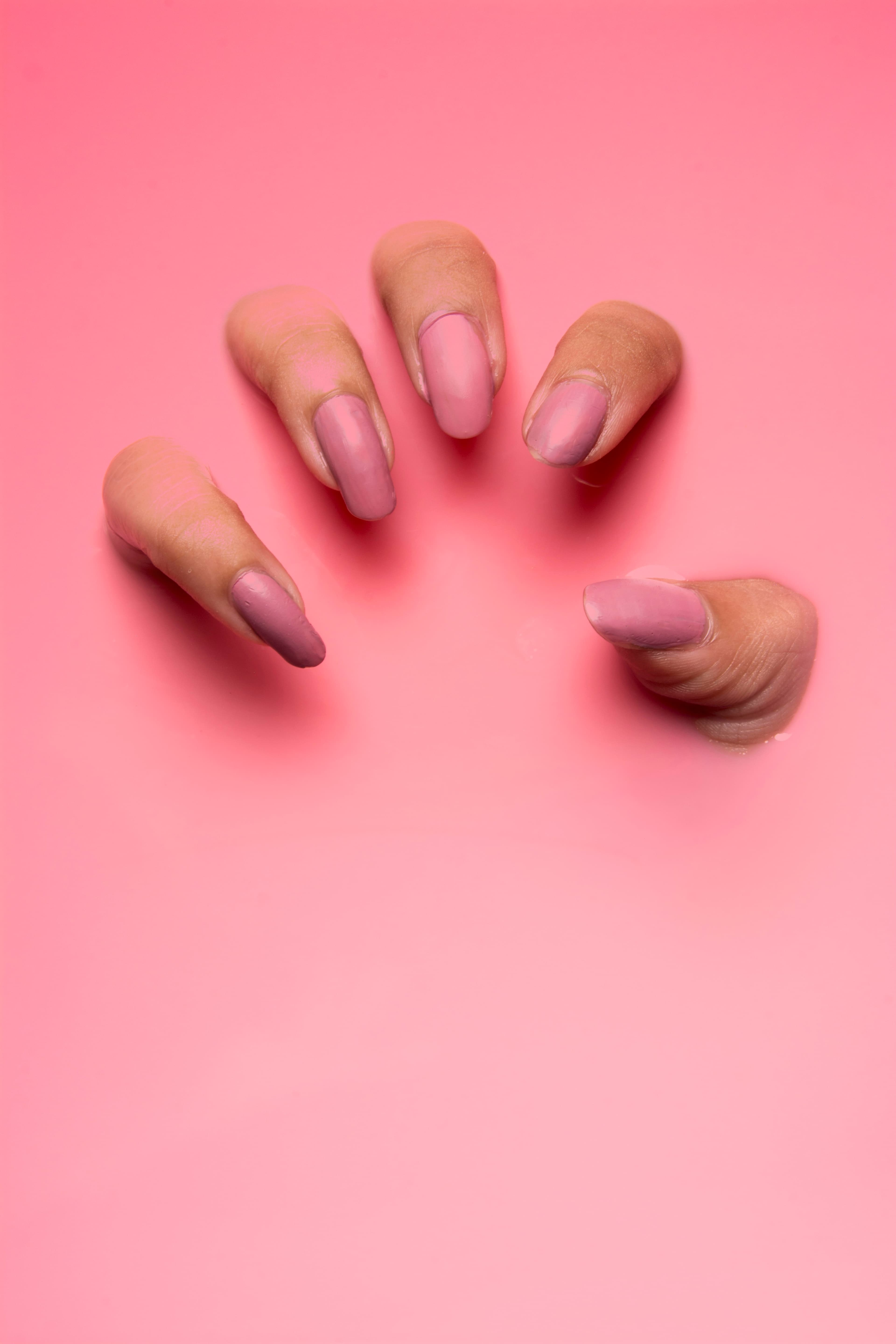 A manicured hand photographed on a pastel pink surface